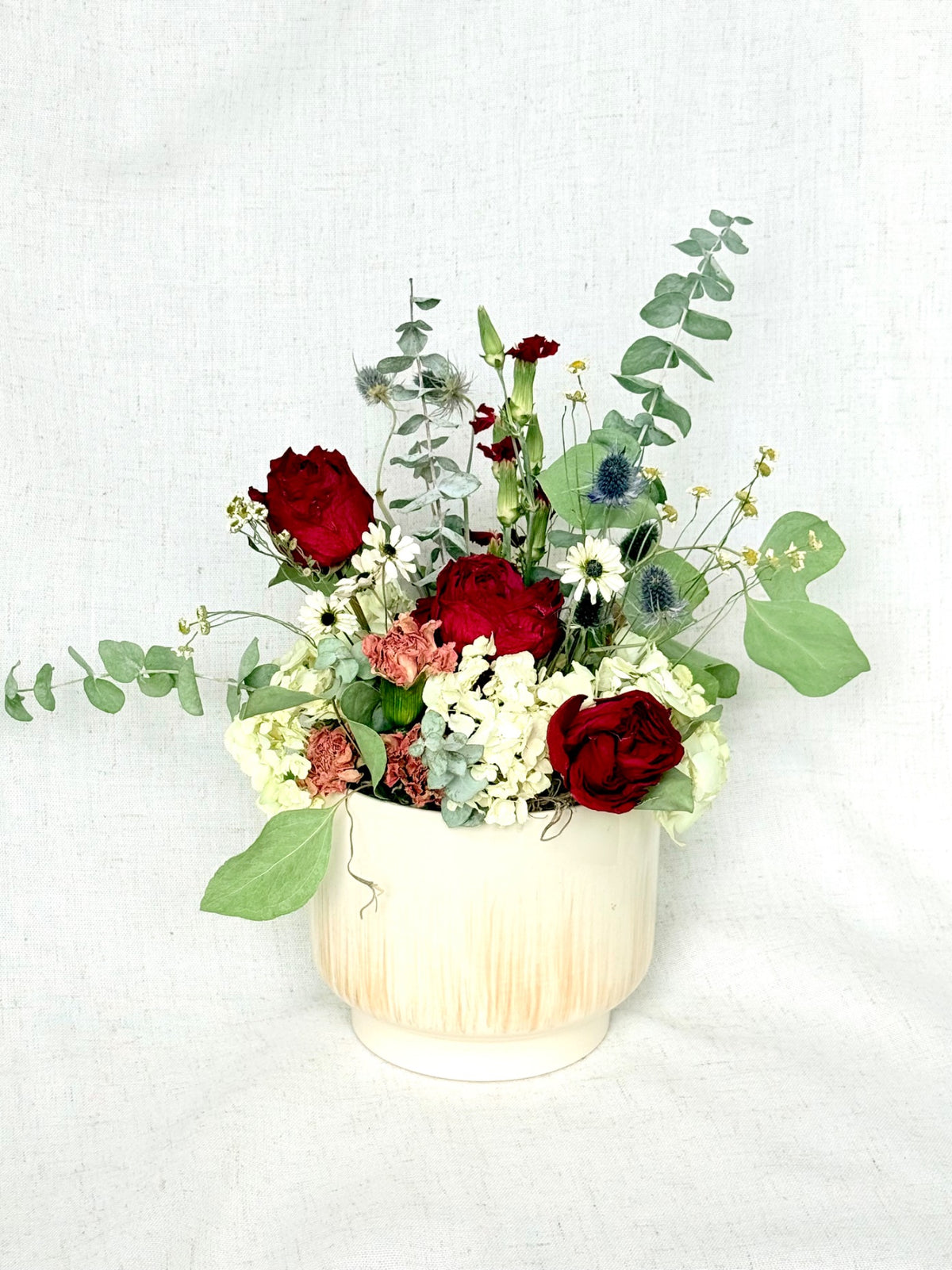 Everlasting Romance arrangement with deep red roses, ivory flowers, and greenery in an ivory vessel