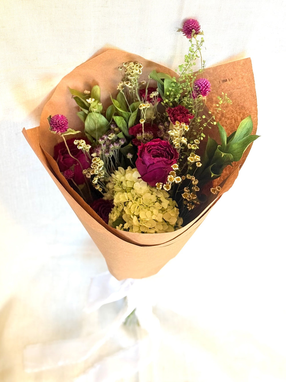 Gathered Meadow dried bouquet wrapped in brown paper with berry roses, pale blooms, and greenery