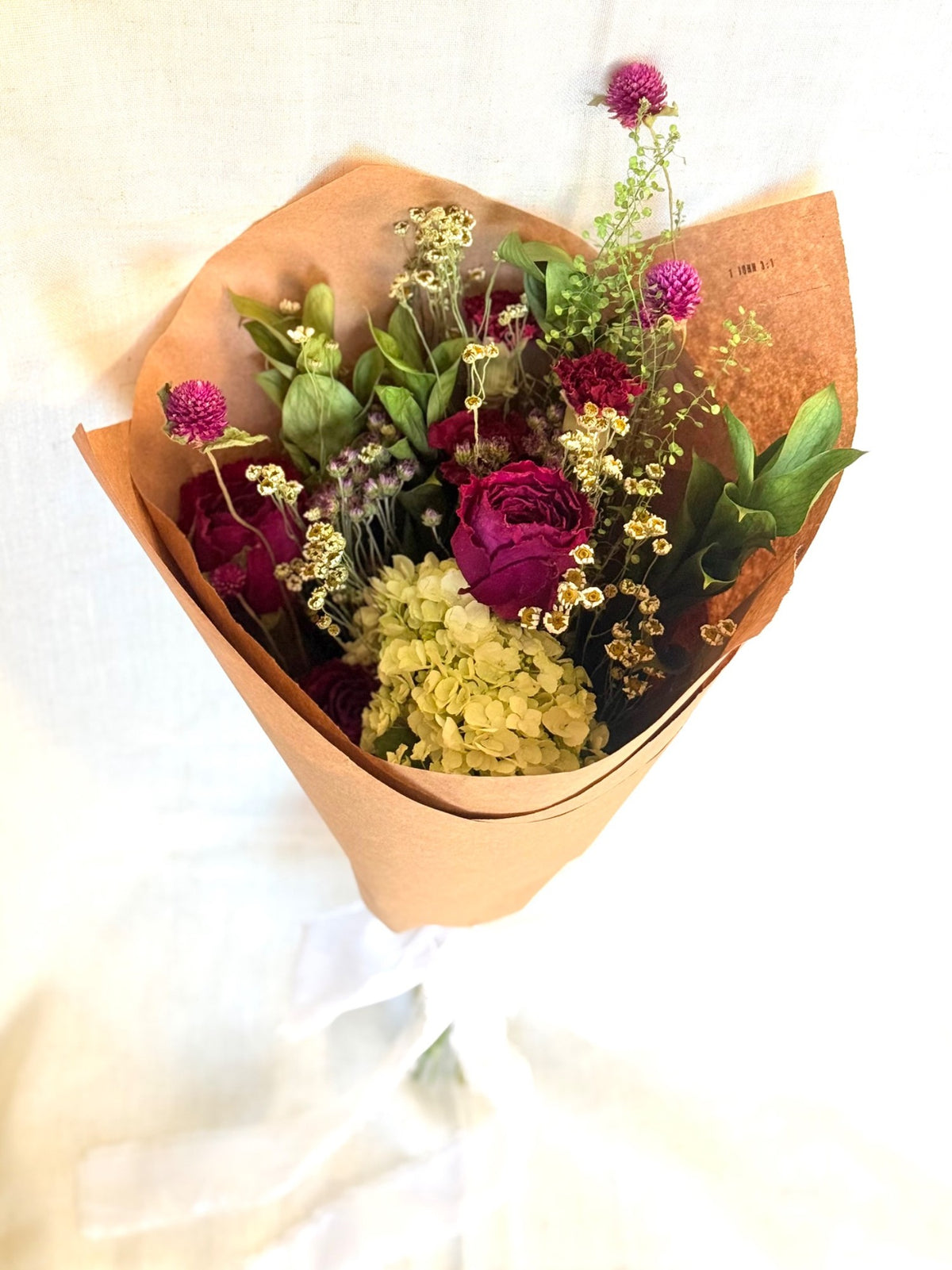 Gathered Meadow dried bouquet wrapped in brown paper with berry roses, pale blooms, and greenery